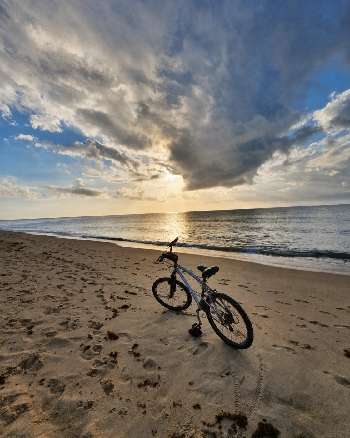 Bicicleta sobre la arena de la playa de Araçaípe, con el mar tranquilo y el sol entre nubes.