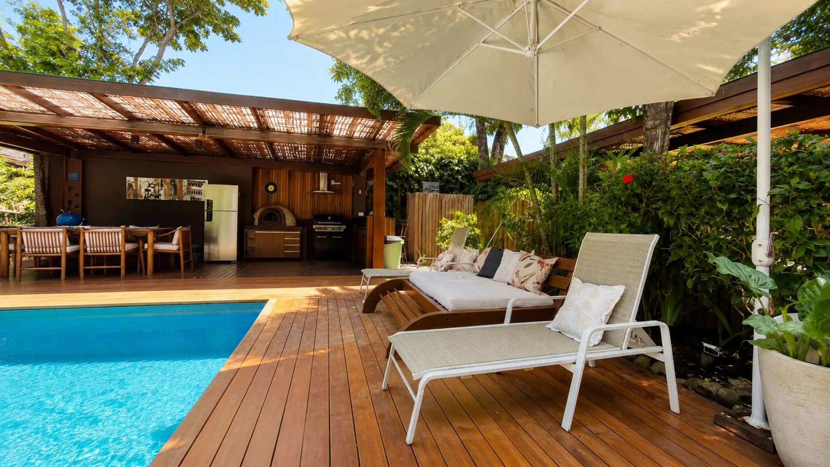 Deck da piscina da Casa Paraíso ao entardecer, com pergolado