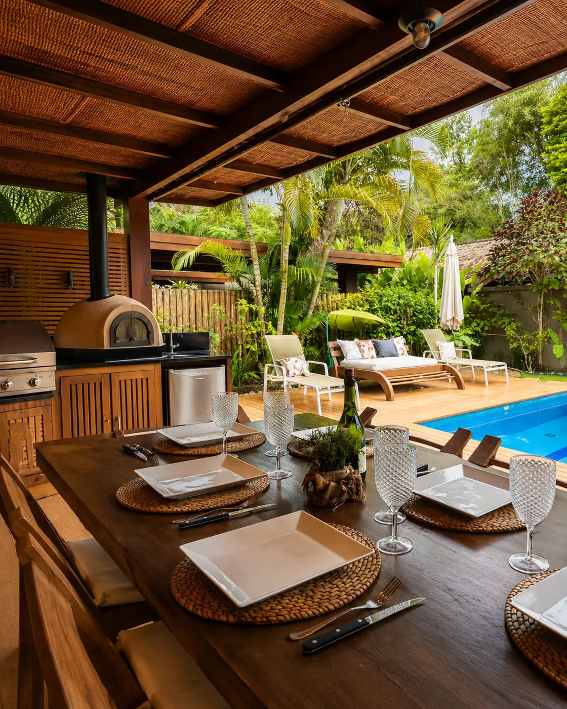 Área gourmet ao ar livre da Casa Paraíso com forno, espreguiçadeiras e piscina