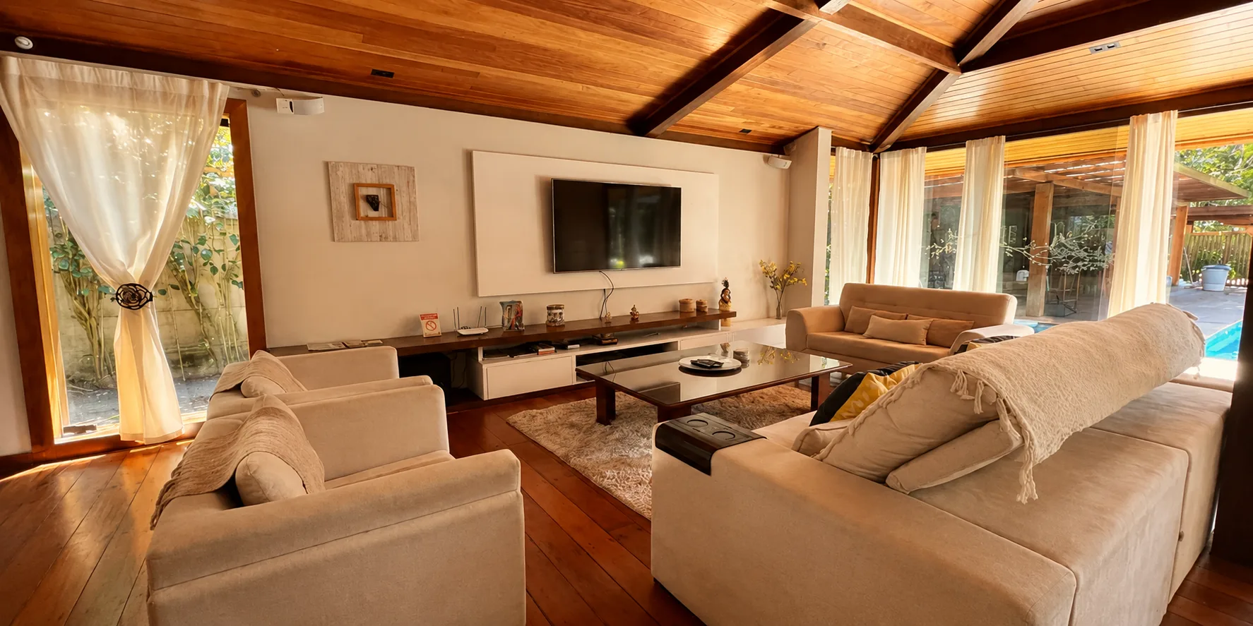 Sala de estar da Casa Paraíso com sofás claros, Smart TV e ambiente climatizado