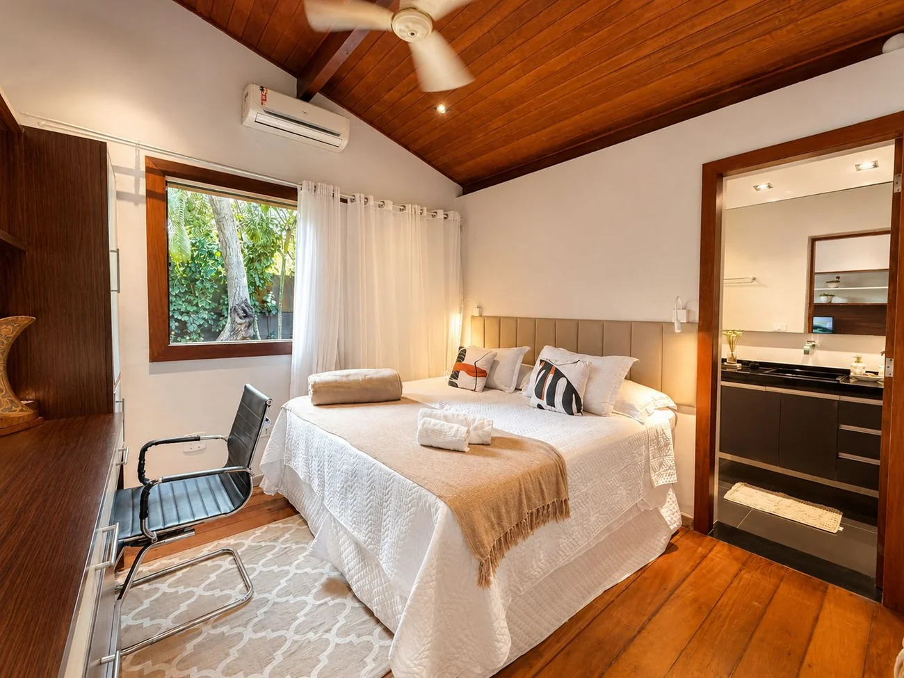 Suíte do térreo da Casa Paraíso com cama queen, banheiro privativo e janela para o verde