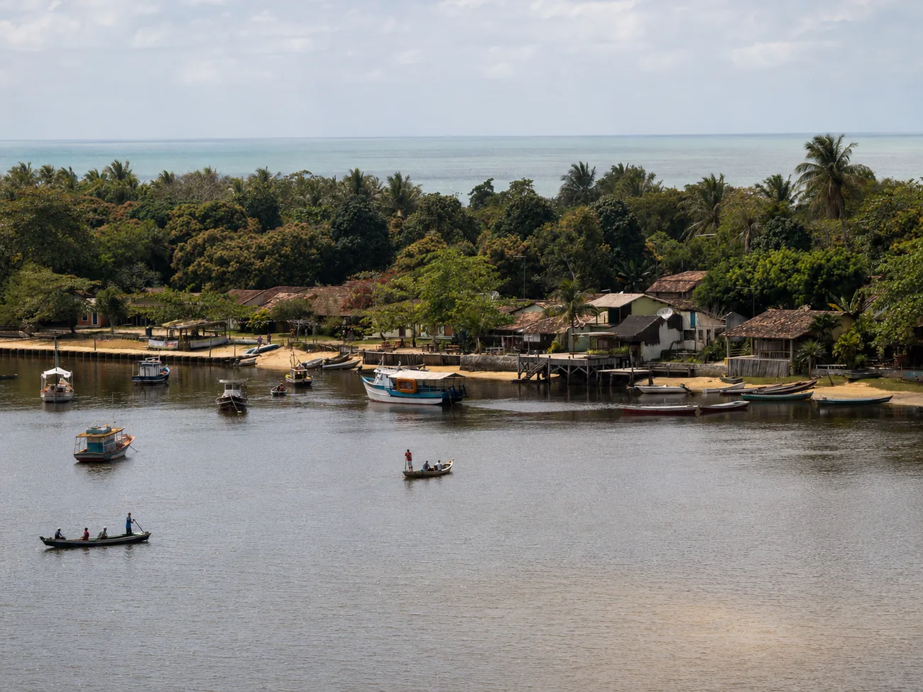 Barcos no rio de Caraíva, com o vilarejo entre os coqueiros e o mar ao fundo