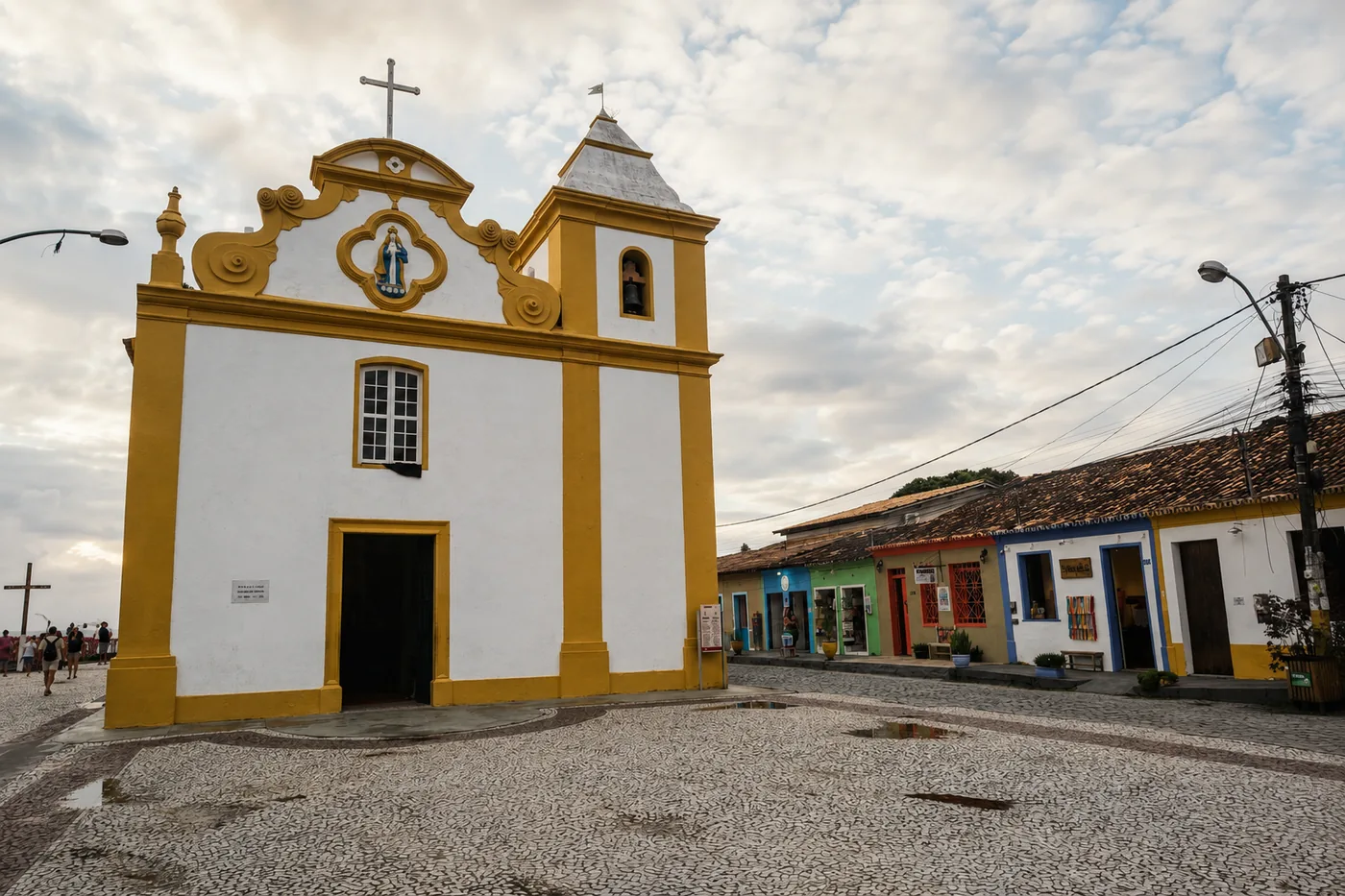 Igreja de Nossa Senhora d'Ajuda, branca e amarela, na praça de pedras do centro histórico de Arraial d'Ajuda