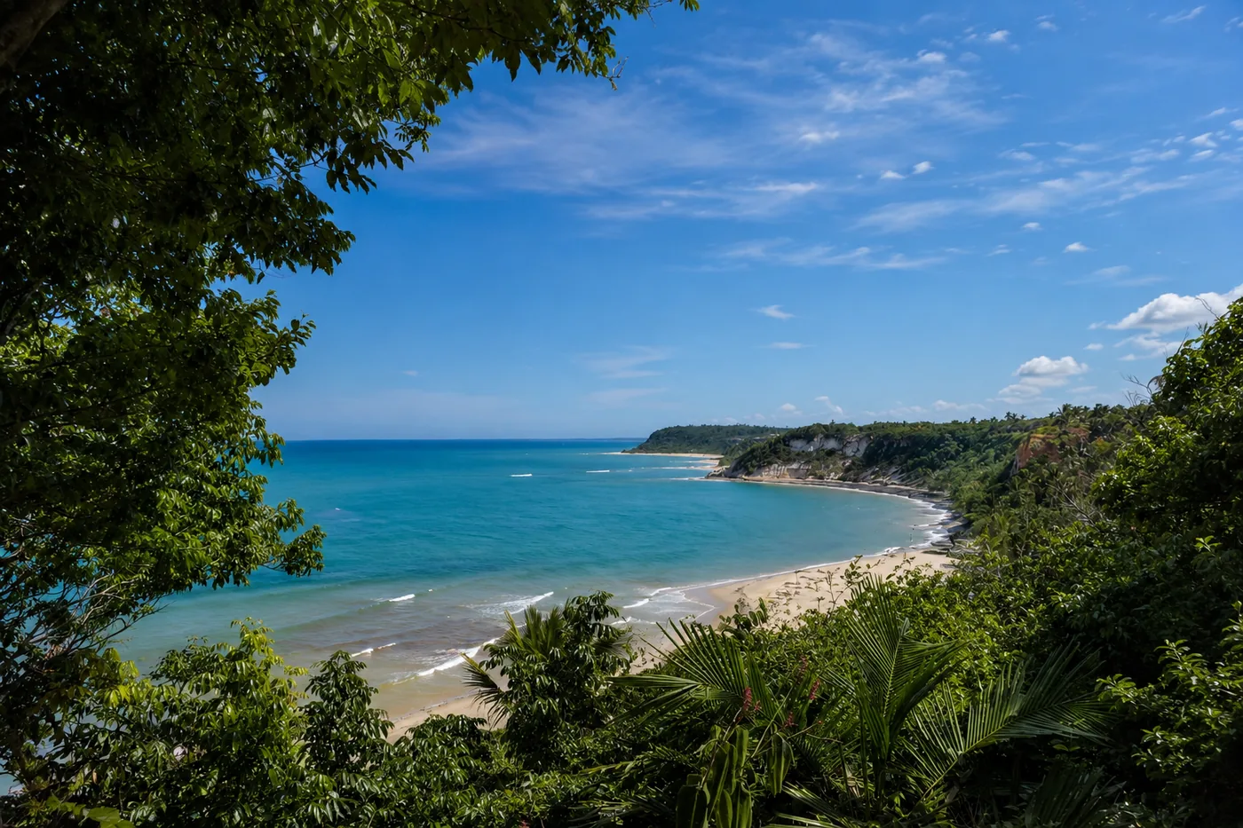 Enseada da Praia do Espelho emoldurada pela vegetação, com mar azul e falésias claras ao fundo
