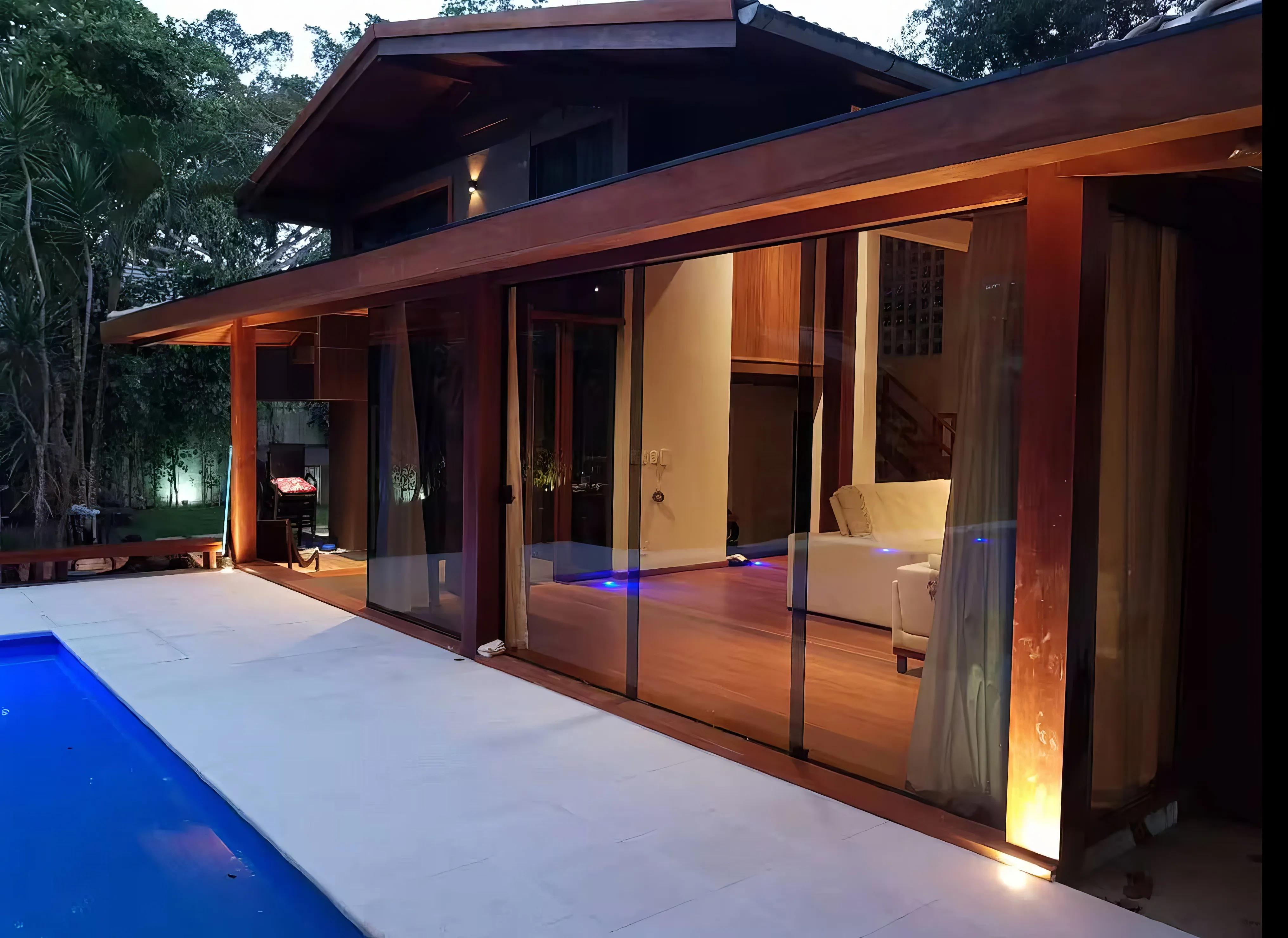 Piscina privativa iluminada ao entardecer, cercada por vegetação.