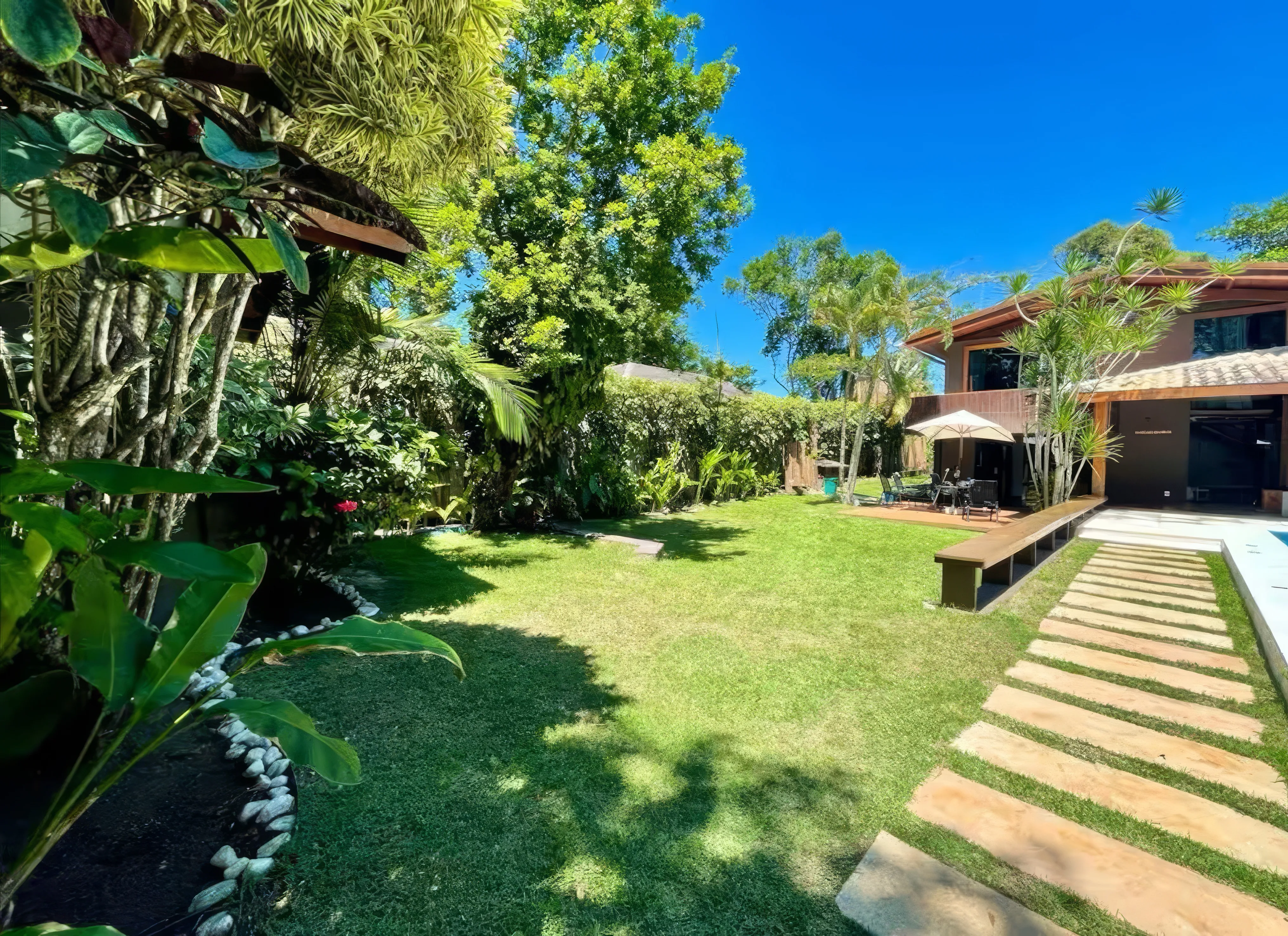 Amplo jardim com paisagismo tropical e piscina privativa ao centro.